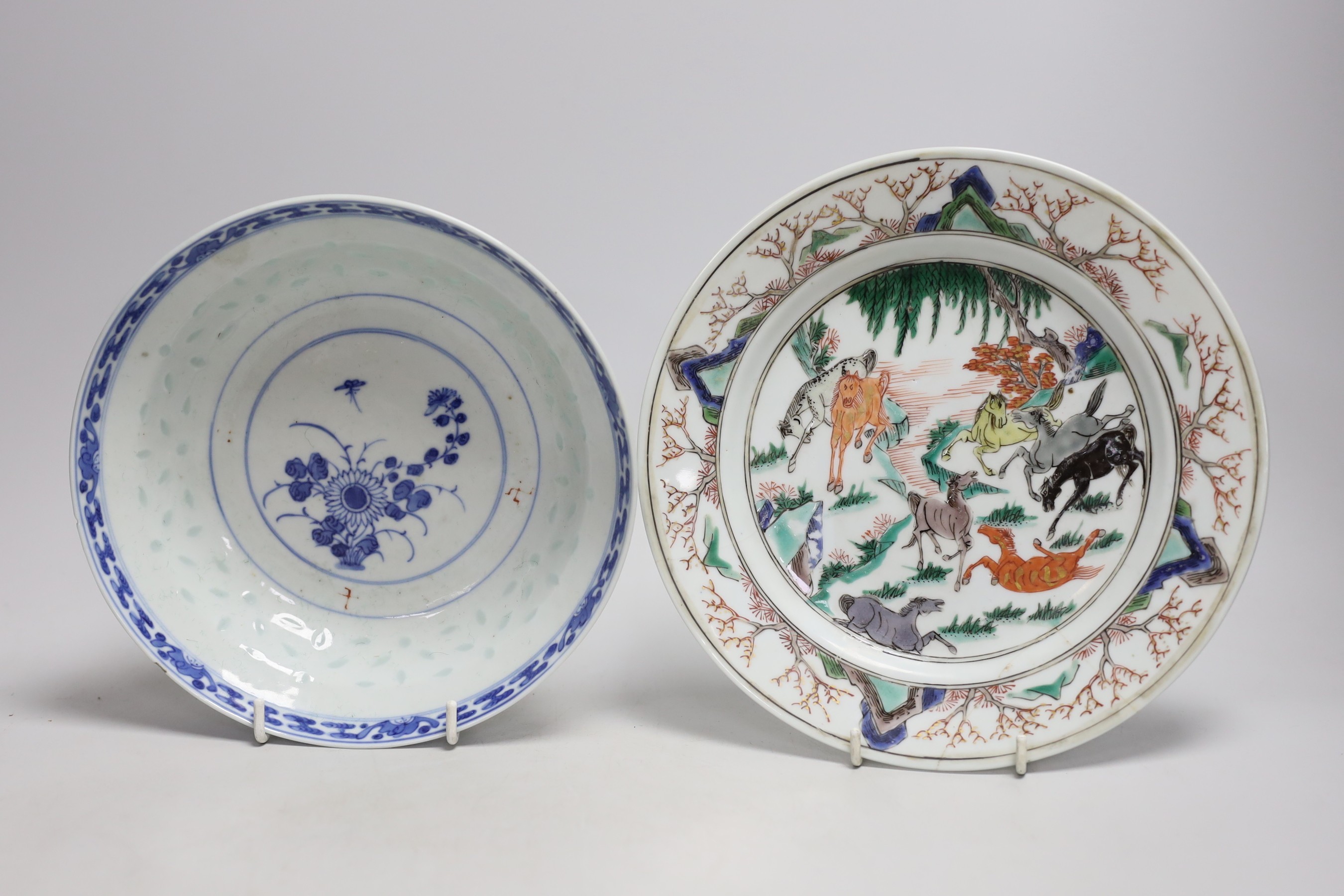 A Chinese famille verte ‘eight horses’ plate, Kangxi period, together with an early 20th century blue and white ‘rice grain’ pattern bowl. Largest 22cm diameter